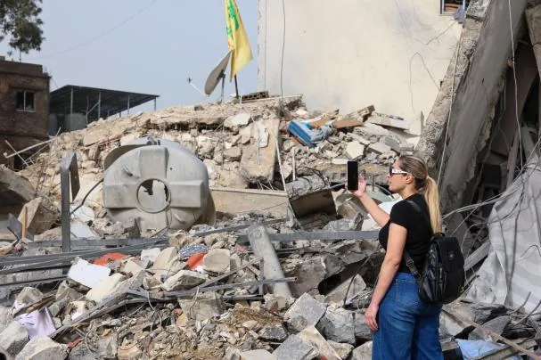 A woman takes a photograph of a destroyed building in the city of Nabatieh, southern Lebanon