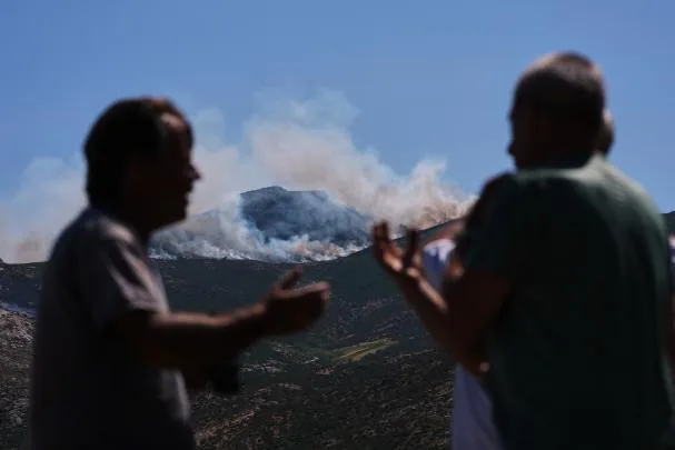 Two neighbors talk as smoke and flames rise near Burgohondo, Ávila province