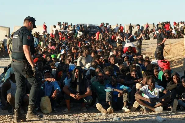 MIgrantes esperan para recibir alimentos en Ceuta vigilados por las fuerzas de seguridad españolas 