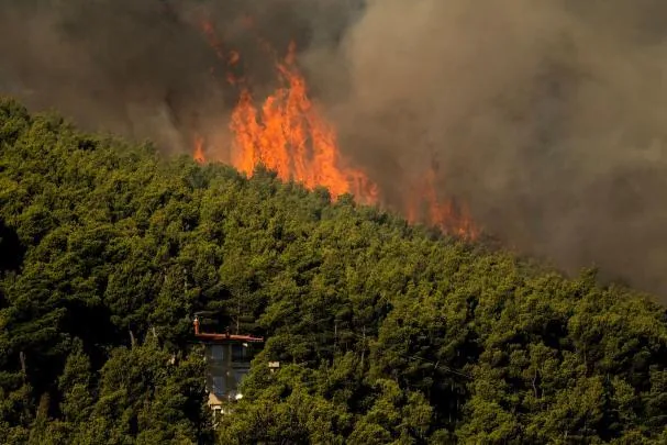 Flames and dense smoke from a forest fire rising over a house in the Porto Germeno area