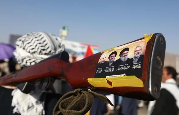 A Houthi supporter carries a weapon with the late leaders of Hamas and Hezbollah